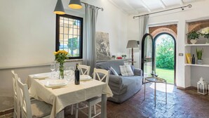 Een eethoek met een tafel voor twee personen, een bank en uitzicht op de tuin door een rondboogvenster.