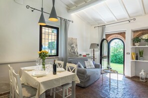 Een eethoek met een tafel voor twee personen, een bank en uitzicht op de tuin door een rondboogvenster.