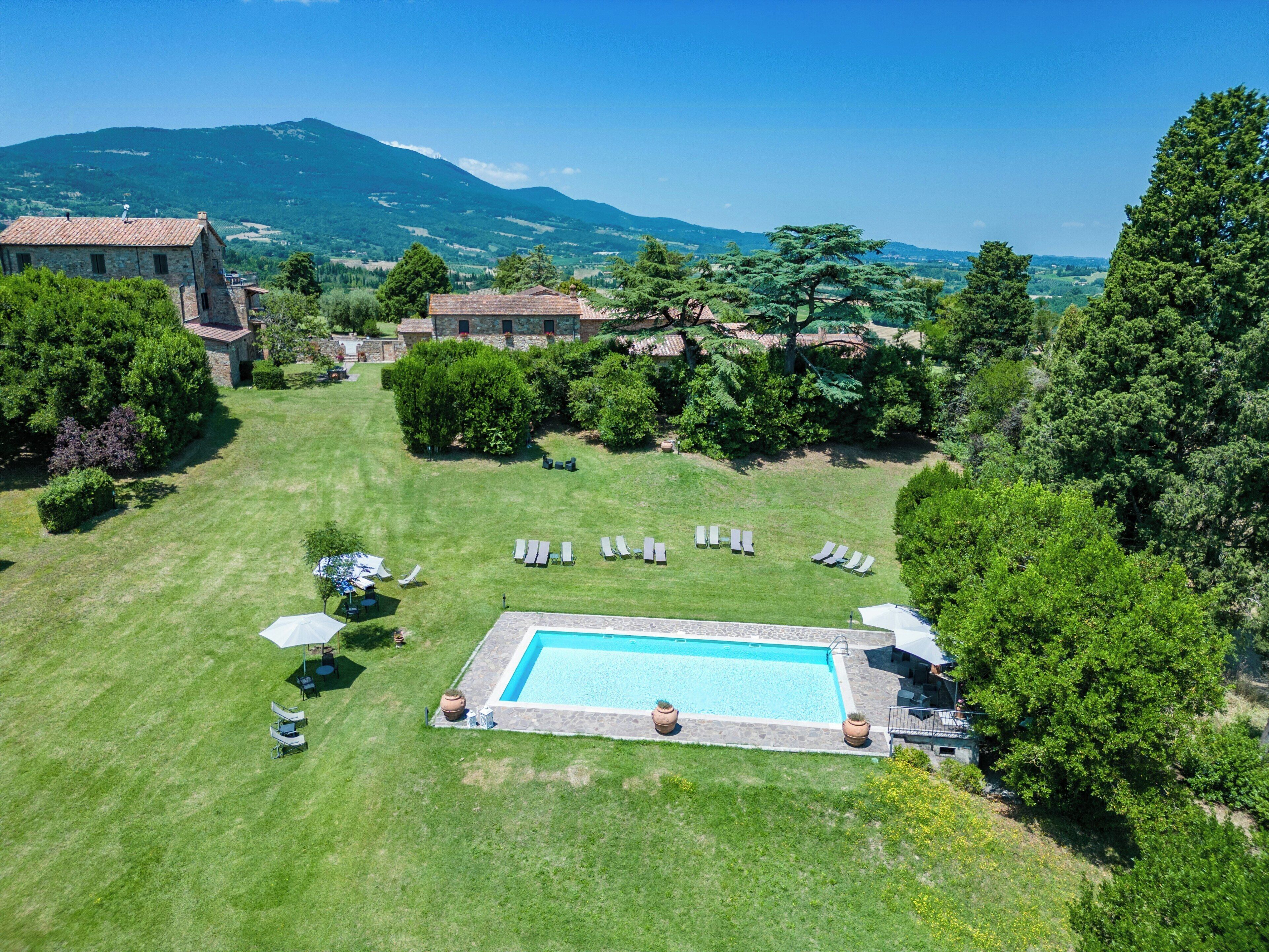 Una piscina envoltada de gandules i ombrel·les, amb una muntanya al fons.