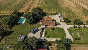 Ovenfra ses en ejendom med swimmingpool, solpaneler og et stort hus med tegltag.