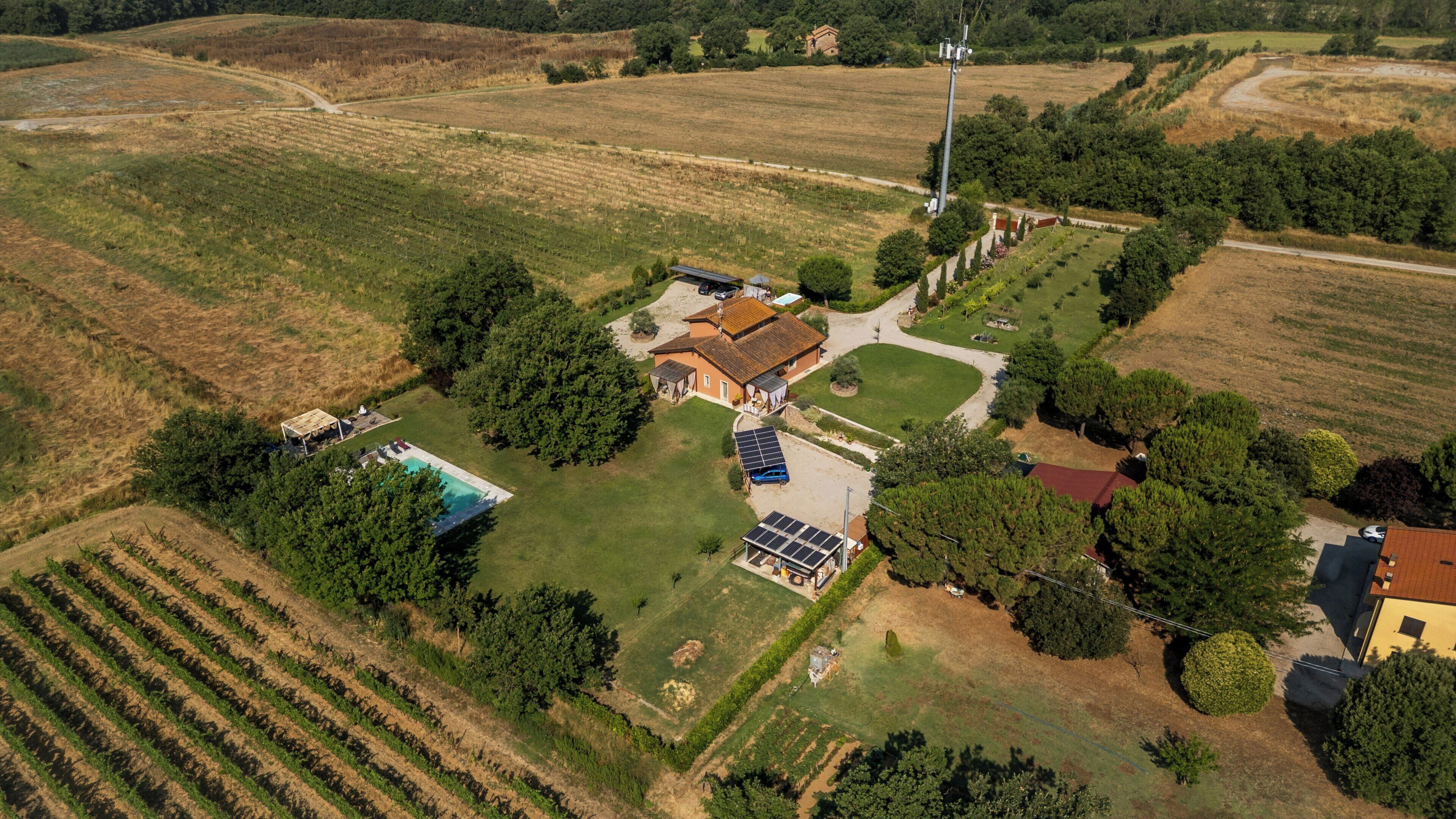An aerial view of a property with a large house, solar panels, a swimming pool, and surrounding agricultural fields.