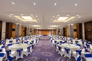 Ein grosser, gut beleuchteter Konferenzraum mit Tischen und Stühlen, einem gemusterten Teppich und einem modernen Deckenstil.