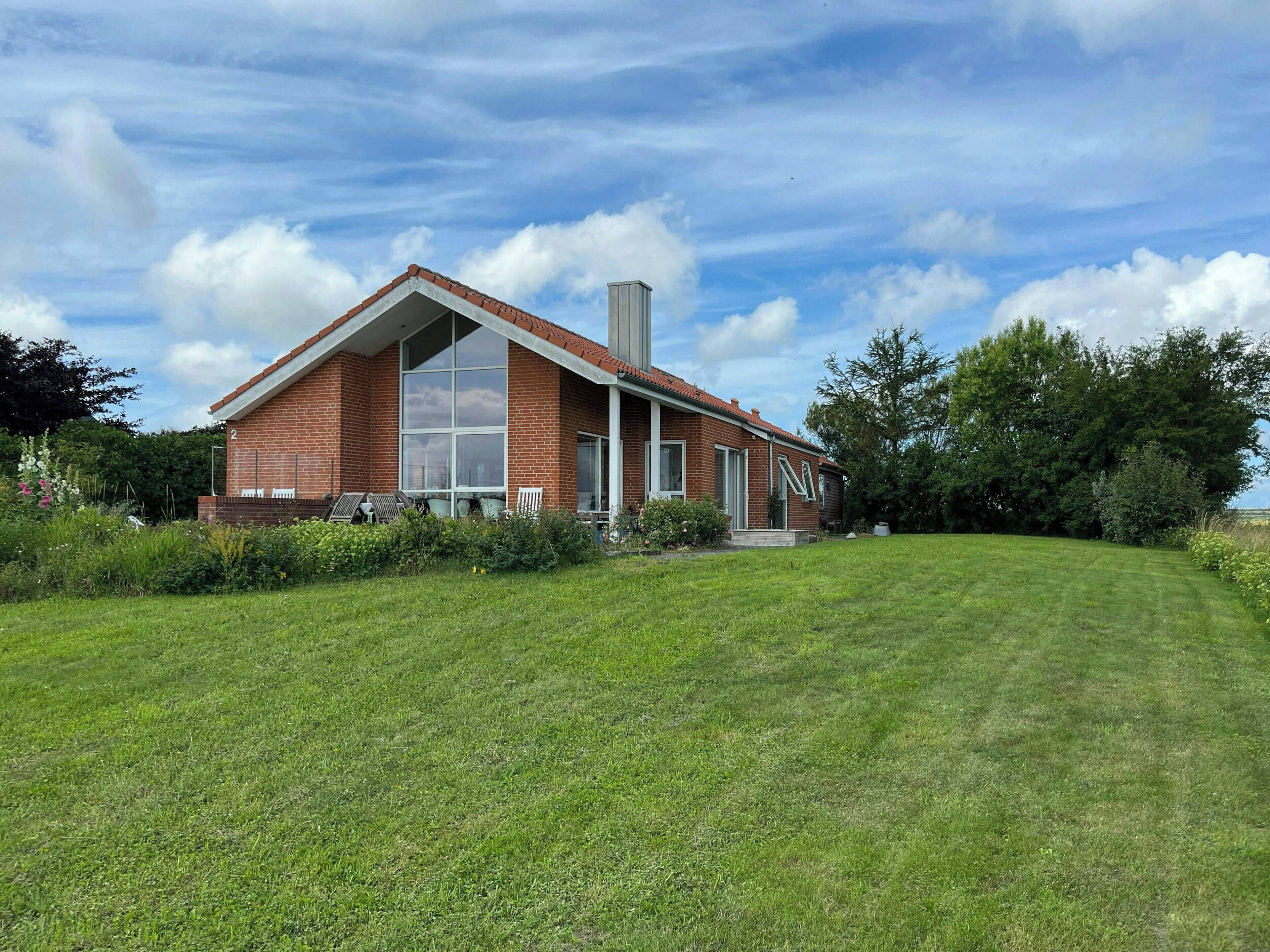 A single-story brick house with a large window, a chimney, and a well-maintained lawn.
