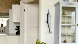 Un coin repas comprenant une table en bois, des chaises, une décoration en forme de poisson, un meuble avec des portes en verre et un vase contenant des plantes séchées.