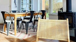 Un coin repas avec une table en bois, des chaises noires, un tapis en fausse fourrure blanche et un fauteuil en osier.