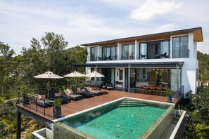 Ein modernes, zweistöckiges Haus mit Dachterrasse, Swimmingpool und Außenmöbeln.