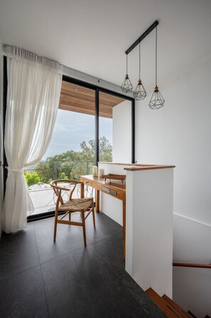 Ein modernes Zimmer mit großem Fenster, einem Holztisch, einem Stuhl und hängenden Pendelleuchten.