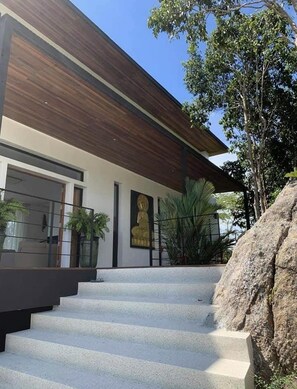 Ein modernes Gebäude mit einem holzverkleideten, geneigten Dach, einer großen Buddha-Statue und einer Treppe, die zum Eingang führt.