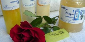 Vier Flaschen HERMANUS Duschgel und Shampoo, eine rote Rose und ein grüner Seifenriegel.