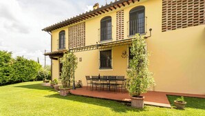 A two-story building with a yellow facade, a balcony with a wrought iron railing, and a patio area with a table and chairs. - Countryside home with pool near Florence (Castelfiorentino)