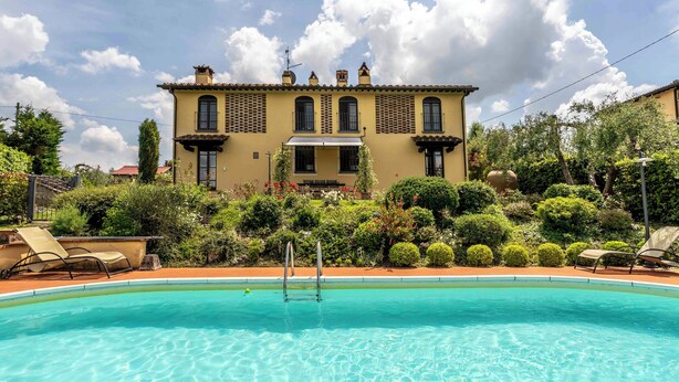 A pool with lounge chairs, a building with multiple windows and balconies, and lush greenery. - Countryside home with pool near Florence (Castelfiorentino)