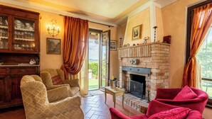 A living room with a fireplace, two armchairs, a wooden cabinet with glassware, and a view through a glass door. - Countryside home with pool near Florence (Castelfiorentino)