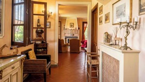 A hallway with a fireplace, wicker furniture, and framed pictures on the walls. - Countryside home with pool near Florence (Castelfiorentino)