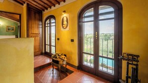 A room with a wooden ceiling, large arched windows, a door with a glass panel, and a table with flowers. - Countryside home with pool near Florence (Castelfiorentino)