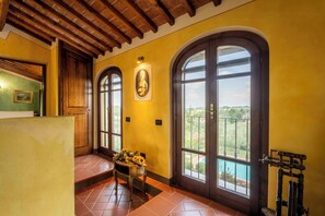 Una stanza con soffitto in legno, ampie finestre ad arco, una porta con pannello in vetro e un tavolo con fiori.