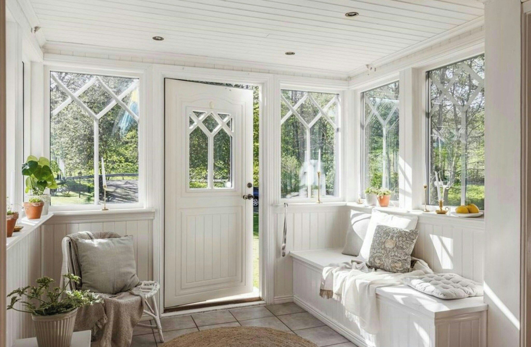 A room with a white door, a bench, and a window with a view of greenery.