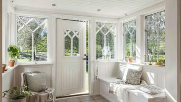 A room with a white door, a bench, and a window with a view of greenery.