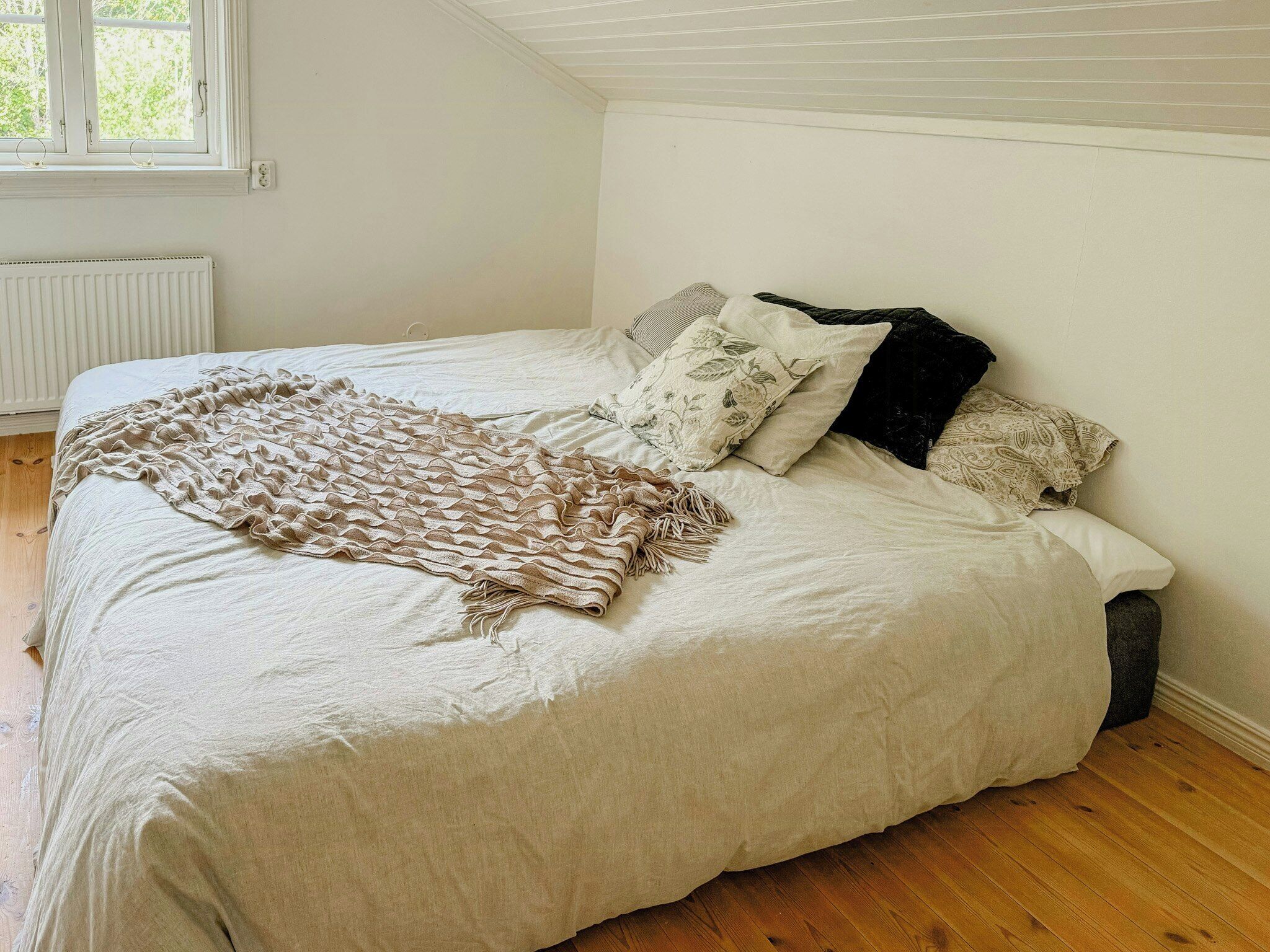 A bedroom with a bed, pillows, a blanket, a radiator, and a window.