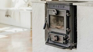 Un interior rústico con chimenea de piedra con la etiqueta 'MORSS', vigas de madera y una habitación de paredes blancas con una ventana.