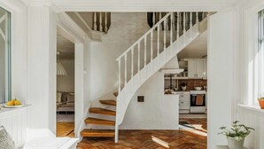 Una escalera que lleva a una cocina con armarios blancos y piso de baldosas.