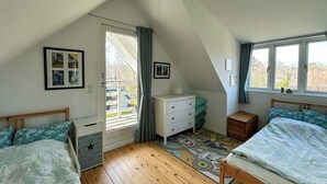 Une chambre avec deux lits, une commode, un bureau, une fenêtre et une porte donnant sur un balcon.