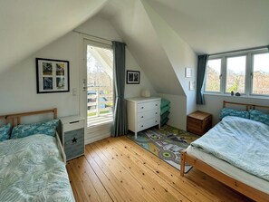 Un dormitorio con dos camas, un aparador, un escritorio, una ventana y una puerta que da a un balcón.