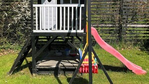 Une cabane en bois pour enfants avec un toboggan rouge et une balustrade blanche.