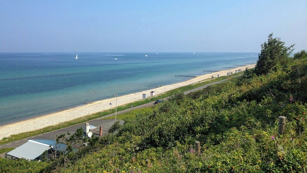 Une vue côtière comprenant une plage, une route et un bâtiment avec un toit bleu.