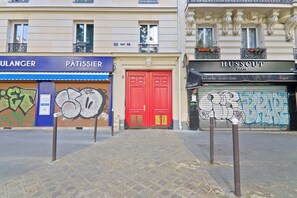 Geschäfte mit heruntergelassenen Rolläden, eine rote Tür und eine Kopfsteinpflasterstraße.