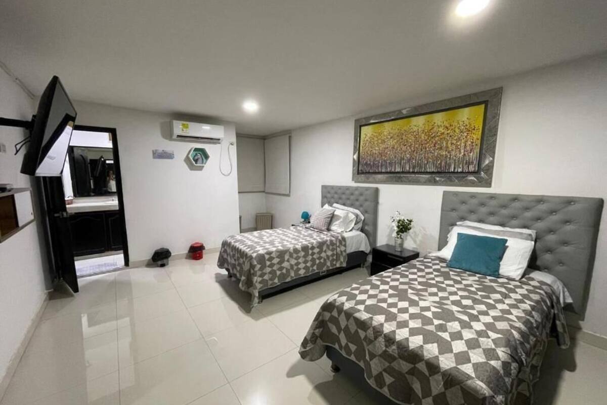 A bedroom with two beds, a flat-screen TV, an air conditioning unit, and a painting on the wall.