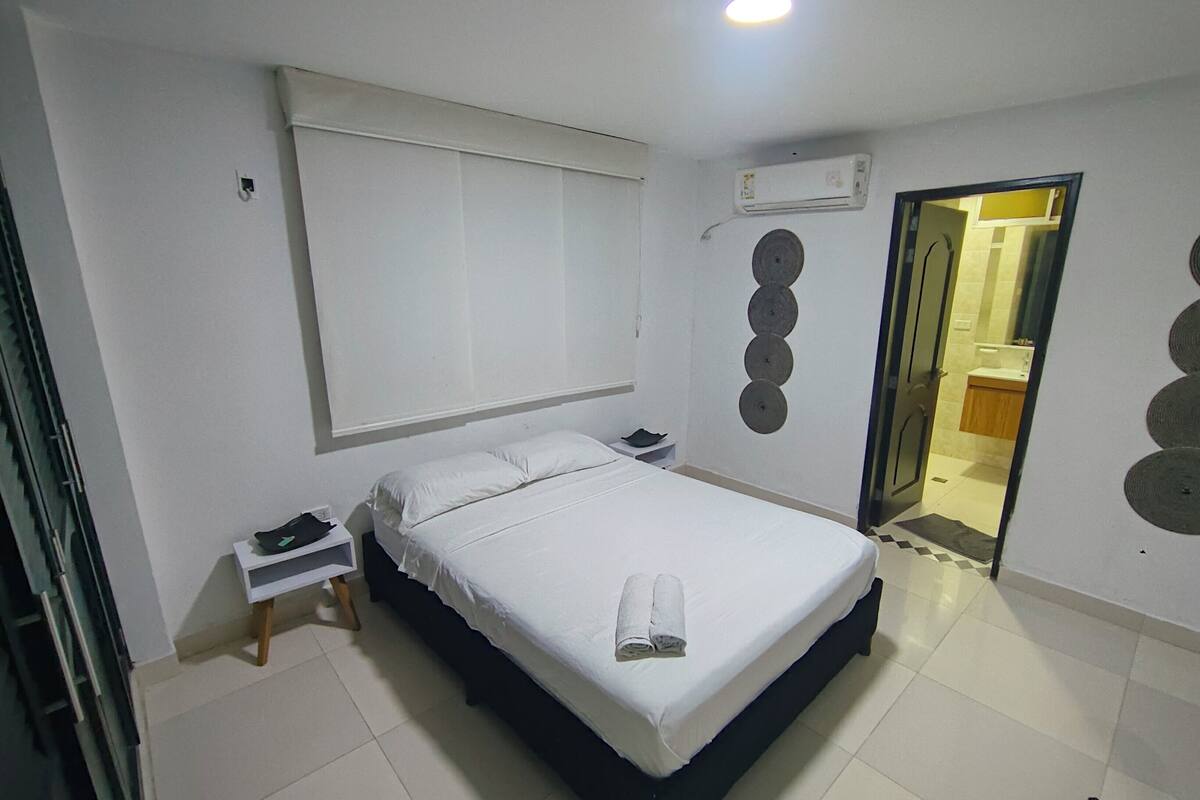 A hotel room with a bed, bedside table, and a mirror.