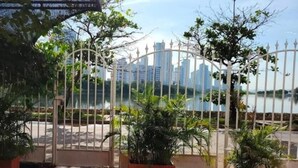 A gated area with potted plants, a view of a body of water, and high-rise buildings in the background.