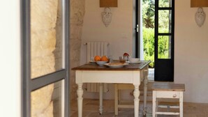 A dining table with a bowl of oranges and a plate, a small stool, and a window with a view of greenery. - pool villa among ancient olive trees in Ostuni (Ostuni)