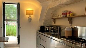 A kitchen with stone walls, a built-in stove, and a window with an open door. - pool villa among ancient olive trees in Ostuni (Ostuni)