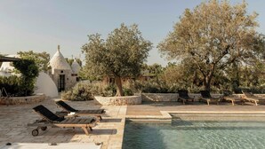 A pool area with lounge chairs, a stone building, and trees. - pool villa among ancient olive trees in Ostuni (Ostuni)