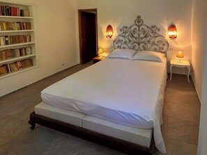 Una cama bien hecha en una habitación con una estantería y dos lámparas de pared.
