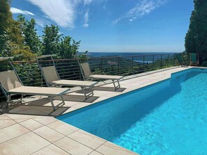 Una piscina con sillas de descanso, una terraza con baldosas y vistas al mar.