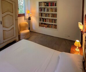 Ein Schlafzimmer mit Bett, Stuhl, Bücherregal und Lampe.