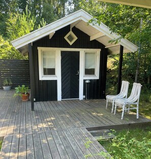 A wooden deck with a black cabin-style building, two white chairs, and a potted plant. - Holiday home by Nyrup Bay and Rørvig harbour (Rørvig)