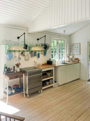 A kitchen with wooden floors, white cabinets, a stove, and various kitchen utensils. - Holiday home by Nyrup Bay and Rørvig harbour (Rørvig)