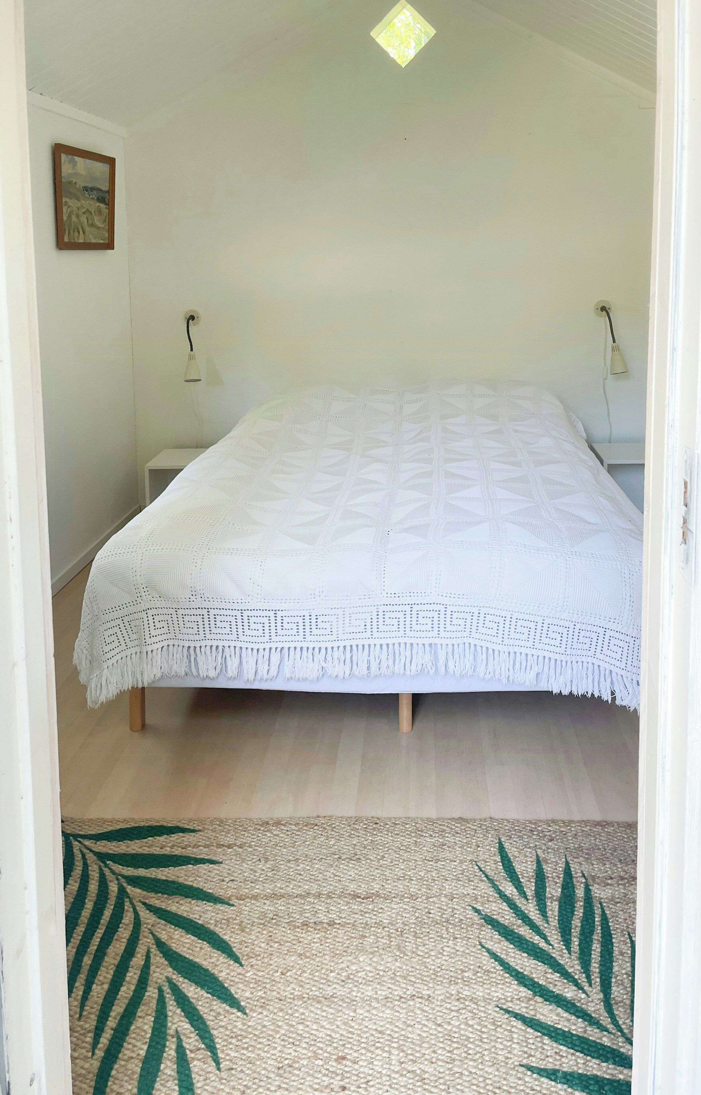 A room with a bed, a nightstand, a lamp, and a wall-mounted light fixture.