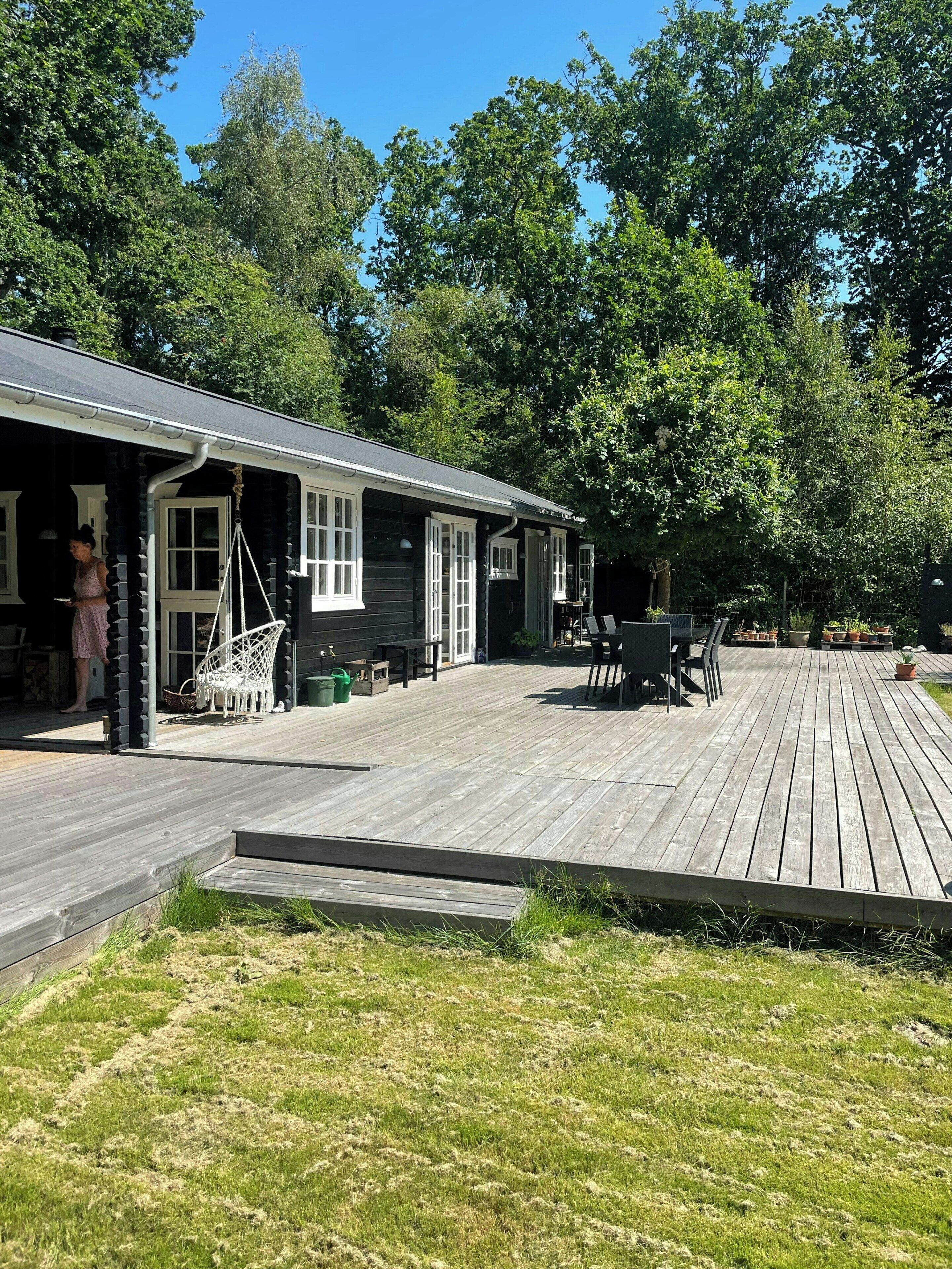 A log cabin with a deck, a swing chair, and a dining table.