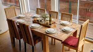 Une table de salle à manger en bois, mise avec des assiettes, des verres et une bouteille, entourée de chaises dotées de coussins à rayures.
