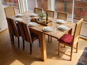 A wooden dining table set with plates, glasses, and a bottle, surrounded by chairs with striped cushions.