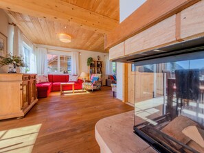 A cozy living room with wooden floors, a red sofa, a glass fireplace, and a view of the outdoors.