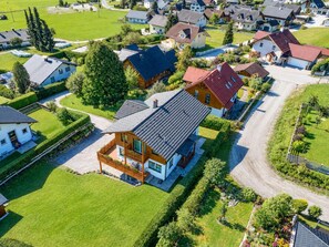 Eine Vogelperspektive auf ein Wohngebiet mit Häusern, grünen Rasenflächen und einem zentral gelegenen, zweistöckigen Haus mit Balkon.