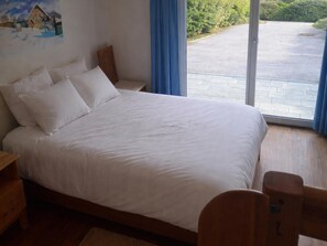 Une chambre avec un grand lit, une table de chevet en bois, une tête de lit en bois et une vue sur une zone pavée, visible à travers une porte vitrée.