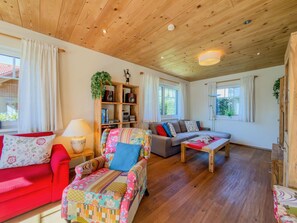 Un salon chaleureux avec un plafond en bois, un canapé rouge, un fauteuil coloré, un canapé gris et une table basse en bois.