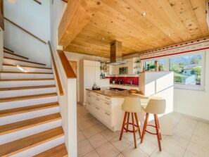 A modern kitchen with wooden beams, white cabinets, and a large island with bar stools.