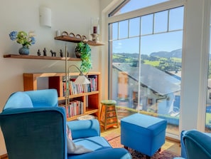 Ein modernes Wohnzimmer mit großem Fenster, blauen Möbeln, einem Bücherregal und Dekoration.